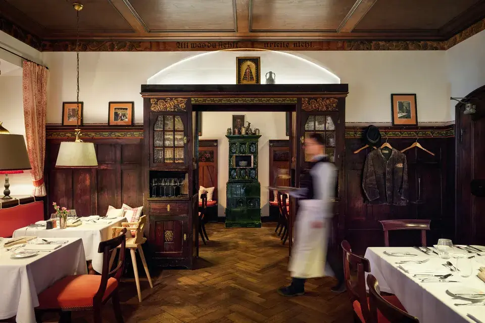 “Alte Stube” Inn with tables and chairs, rustic in style, with a staff member in the foreground