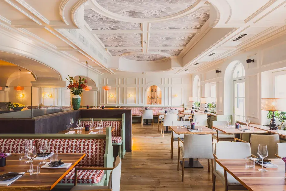 Interior view of Mizu Sushi Bar, featuring a white ceiling with inlays, wooden floors, set tables, and large windows.
