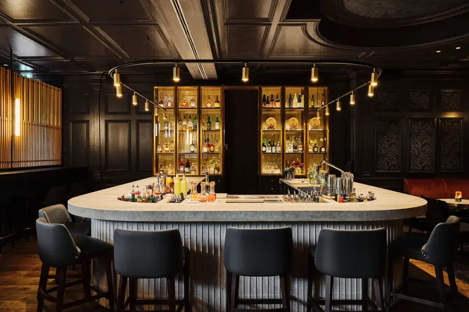 Mizu Bar - A darkly designed bar area at Bachmair Weissach featuring a round counter and illuminated bottle racks.