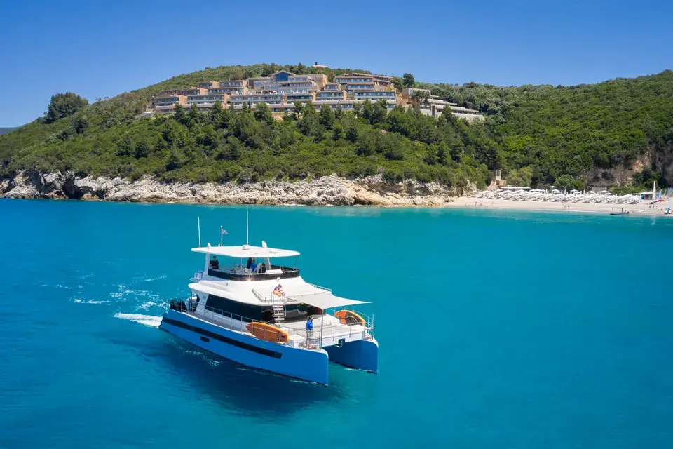 An exclusive catamaran on the Ionian Sea off a forested coastline.