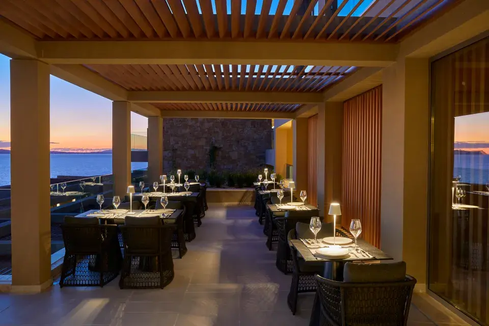 A covered restaurant terrace with set tables and a view of the ocean.