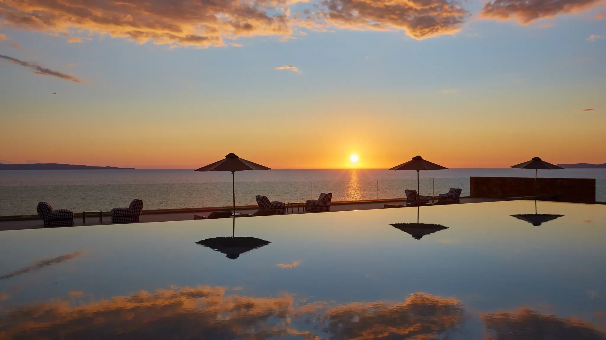 Infinity Pool with sun umbrellas overlooking the Ionian Sea at sunset.