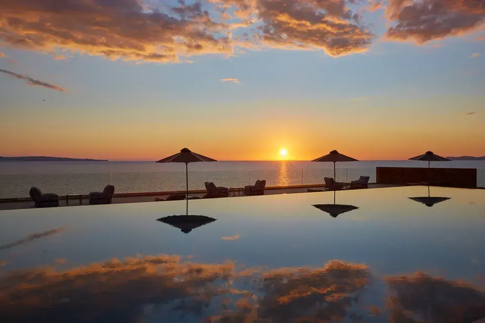 Infinity Pool mit Sonnenschirmen und Blick auf das Ionische Meer bei Sonnenuntergang.