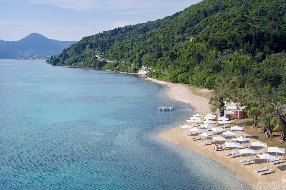 A beach with the ocean, umbrellas, and lounge chairs, with a green coastline in the background