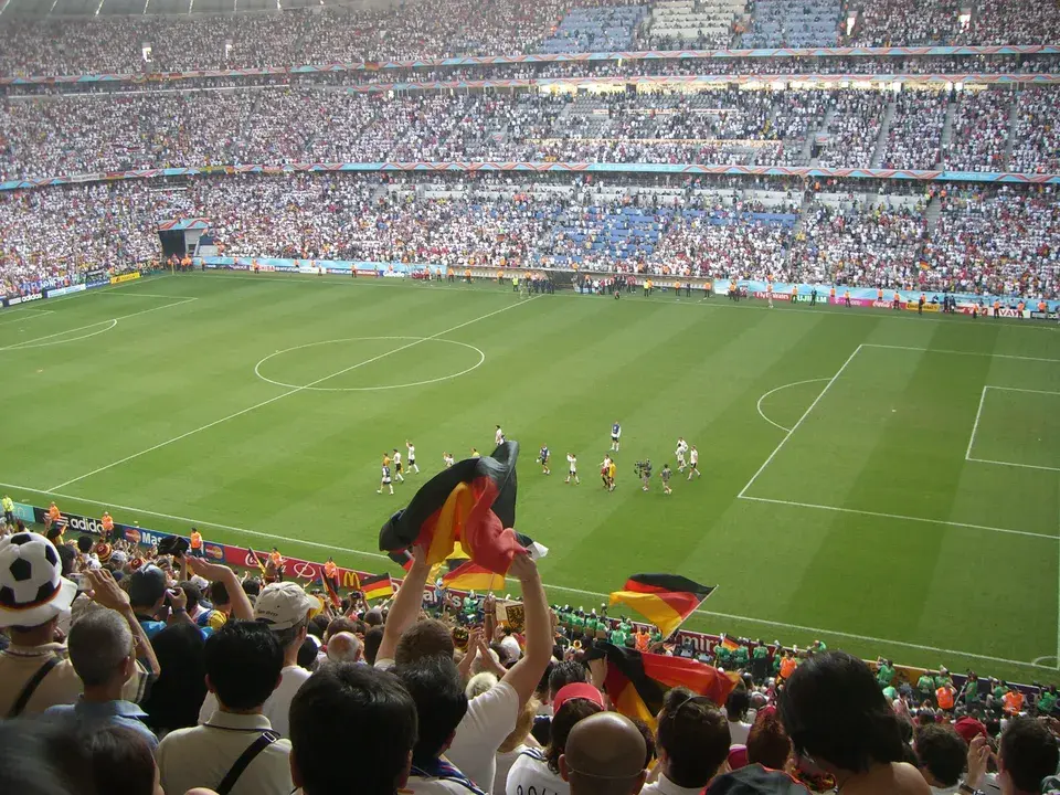 Deutsche Fußballfans mit Deutschlandfahnen auf der Tribüne eines voll besetzten Stadions