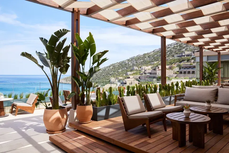 Crystal Box Bar on the beach with palm trees, a covered terrace with seating, lounge chairs, and views of the ocean and the coastal landscape.