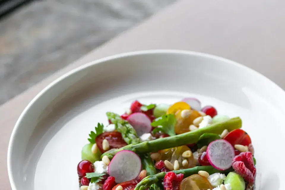 Close-up of a prepared salad with green vegetables, radishes, berries, pomegranate seeds, and other fresh ingredients.