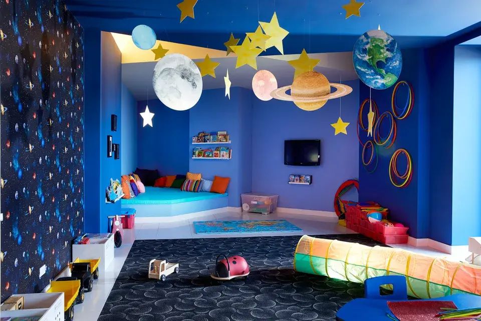 Colorful playroom at the Daios Cove Kids Club with seating and play areas and walls decorated with planets and stars.