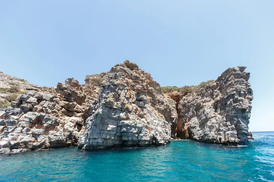 Rock formations along the coast of Crete surrounded by clear turquoise-blue water beneath a blue sky.