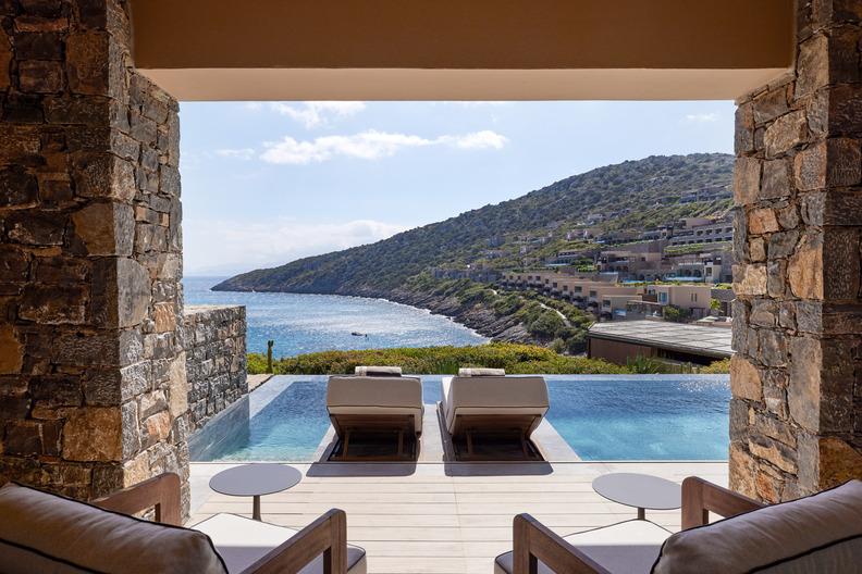 Terrace of an accommodation at Daios Cove with a private pool, two lounge chairs, and views across the bay and the terraced resort.