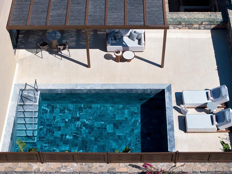 View from above of a private rectangular pool at Daios Cove Premium Junior Suite with an adjoining terrace, outdoor seating, and lounge chairs.
