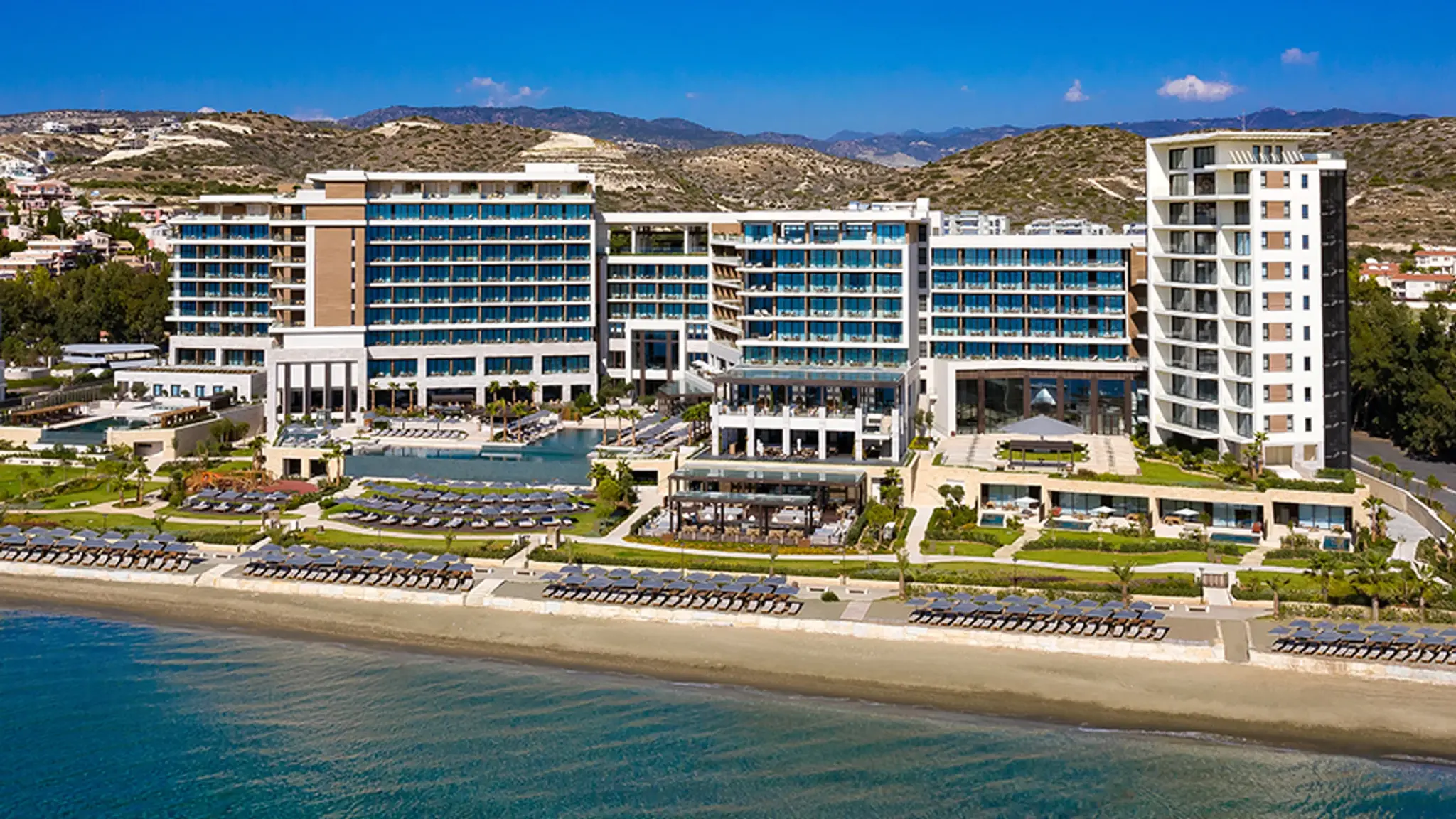 Außenansicht des AMARA auf Zypern mit Hotelgebäude, Poolanlage und Mittelmeer im Vordergrund