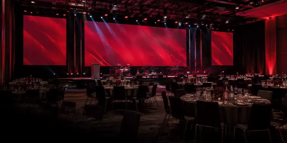 Große Eventbühne in Rot-Weiß und Bildschirmen mit dem FCB Logo mit gedeckten Tischen in Rot-Weiß