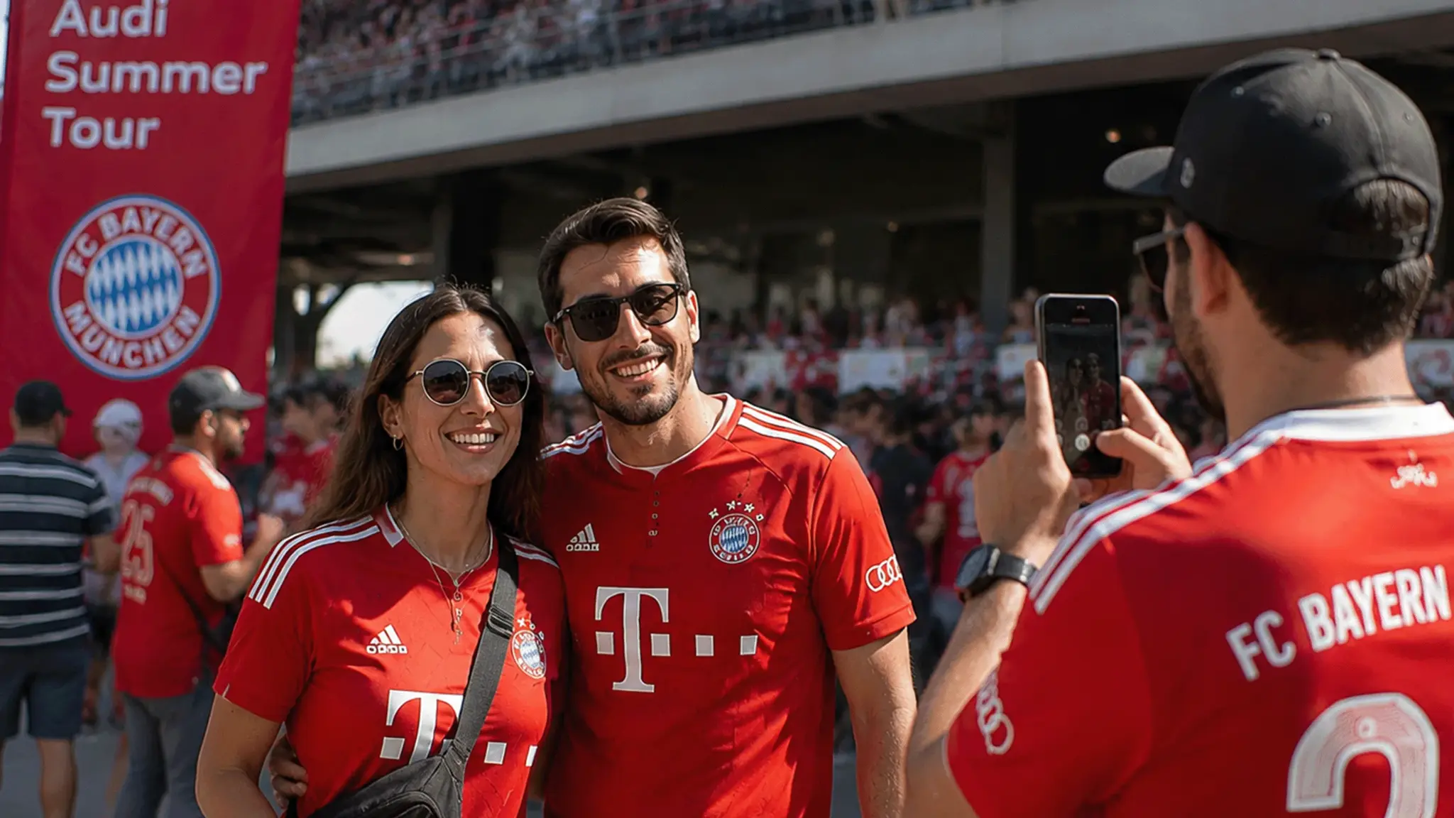 Zwei FC Bayern Fans in Trikots posieren während der Audi Summer Tour für ein Foto, das ein weiterer Fan mit dem Smartphone aufnimmt.