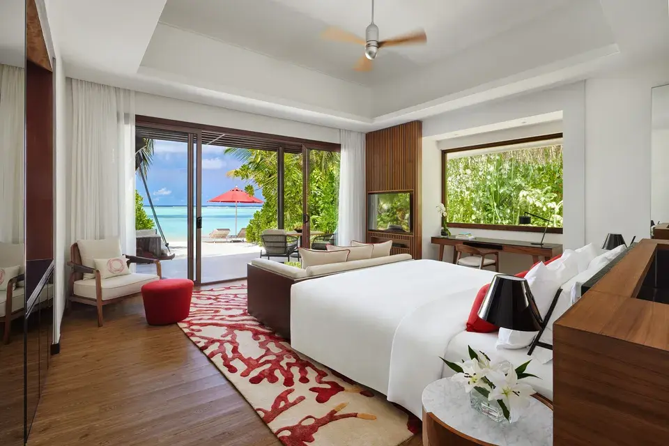 Bright beach villa bedroom at Niyama Private Islands Maldives with a double bed, seating area, and large glass doors overlooking the terrace and tropical greenery.