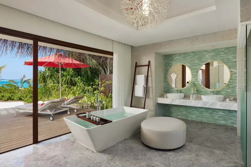 Bright bathroom in the Beach Pool Villa at Niyama Private Islands Maldives, featuring a freestanding bathtub, a sink, and direct access to a landscaped outdoor area.