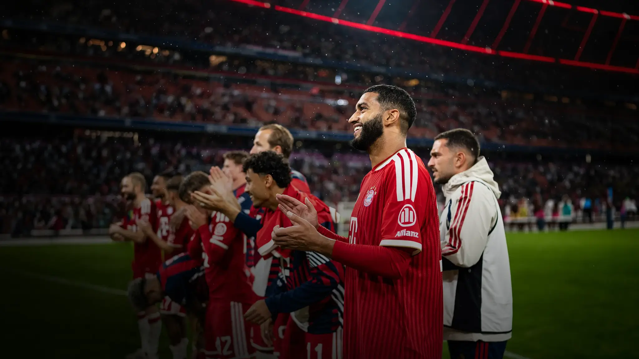 FC Bayern Spieler um Saibari stehen vor Fankurve und applaudieren Fans