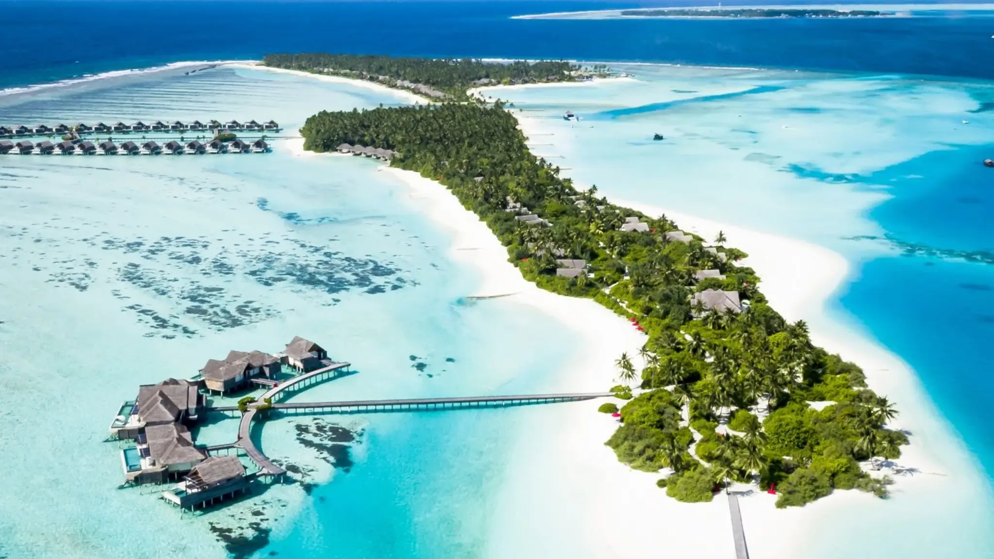 Aerial view of a tropical island at Niyama Private Islands Maldives with a white-sand beach, dense palm trees, a turquoise lagoon, and villas along the water.