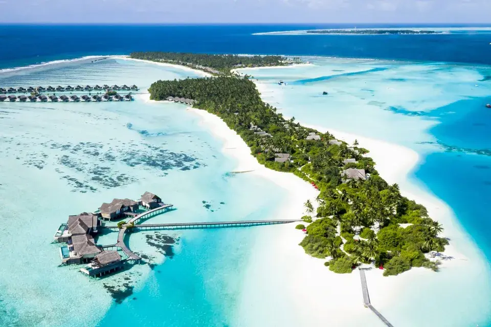 Luftaufnahme einer tropischen Insel des Niyama Private Islands Maldives mit weißem Sandstrand, dichter Palmenvegetation, türkisfarbener Lagune und Villen am Wasser.