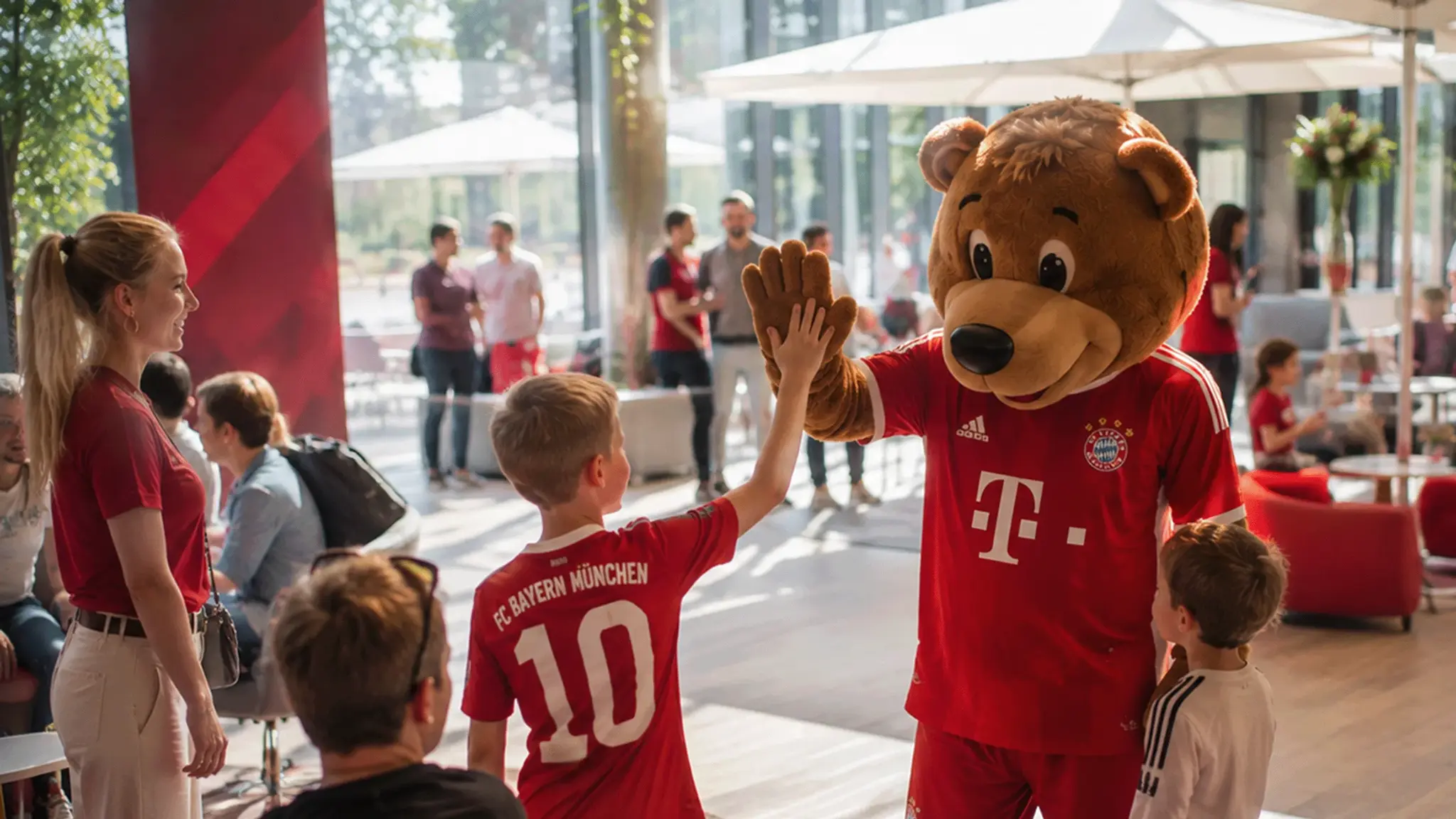 Ein Junge im FC-Bayern-Trikot gibt dem FC-Bayern-Maskottchen Berni bei einer Veranstaltung ein High Five.