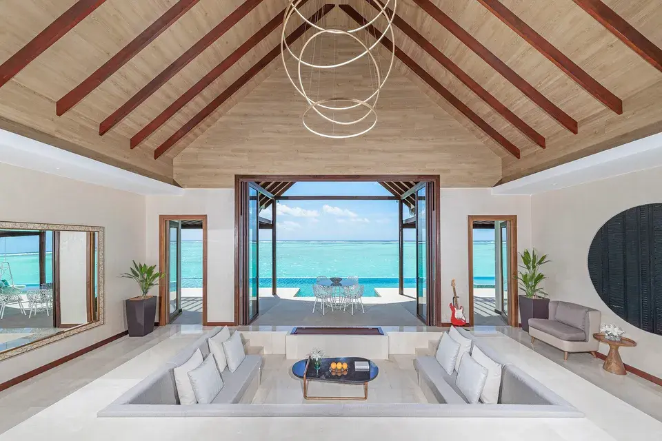Ocean Pool Pavillon: Offener Wohnbereich mit Sitzgruppe und großen Türen, die den Blick auf das türkisfarbene Meer freigeben.